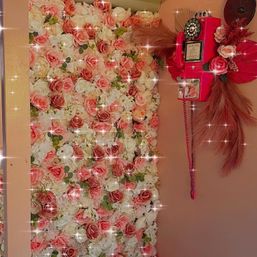 Indoor pink-and-white rose floral wall backdrop with sparkling overlay, paired with a decorative vintage-style red payphone and dried pampas accents — photo-ready decor