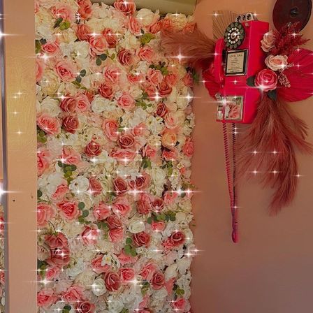 Indoor pink-and-white rose floral wall backdrop with sparkling overlay, paired with a decorative vintage-style red payphone and dried pampas accents — photo-ready decor