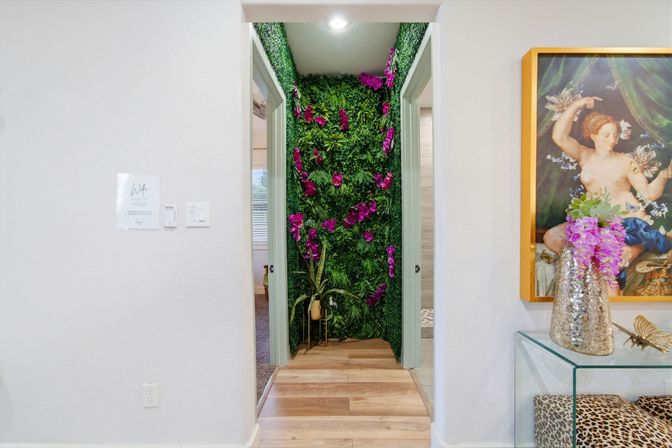 Modern home hallway with an indoor vertical green wall and bright purple orchids in a recessed nook, wood-plank floors, framed classical painting and metallic vase with pink blooms.