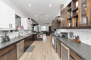 Spacious modern open-concept kitchen with dark wood cabinets, white subway tile backsplash, stainless steel appliances, pendant lights and wood-look flooring leading to a bright living area