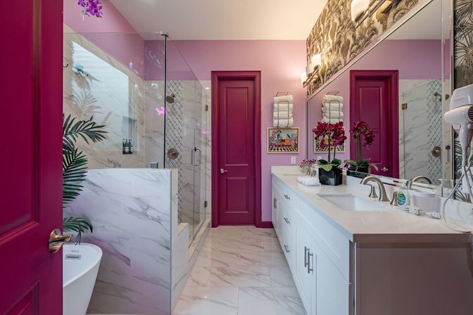 Vibrant pink and magenta luxury bathroom with marble floor and walls, glass walk-in shower, freestanding tub, white double vanity with quartz countertop, chrome fixtures, purple orchids and stacked towels