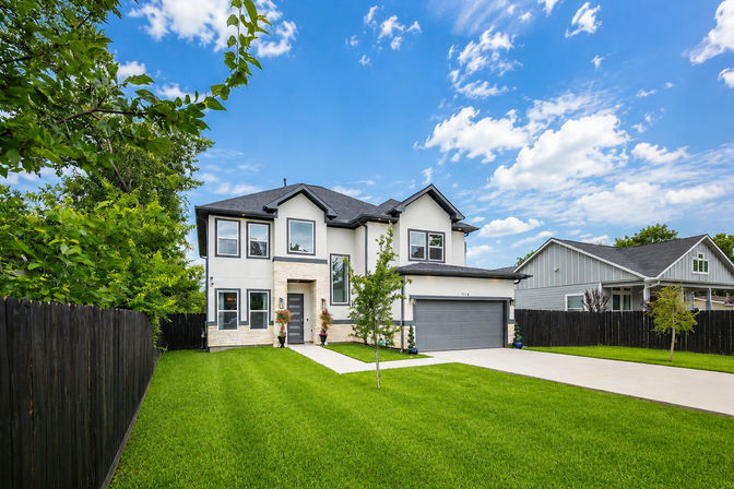 Modern two-story suburban home with a gray double garage, stone-accent entry, manicured green lawn and black fence under a bright blue sky