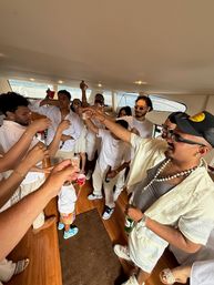 Lively yacht party: group of friends in white outfits raising shot glasses onboard with ocean views, summer celebration vibe.