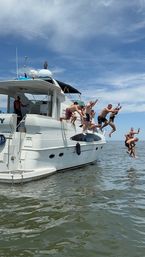 People jumping off a white yacht into calm coastal water under a bright blue sky — lively summer boat party scene