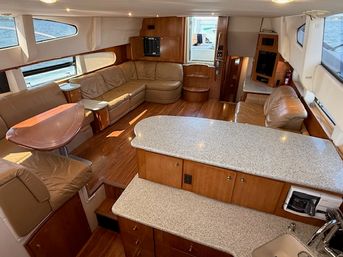 Spacious yacht interior salon with curved tan leather seating, wood floors, rounded dining table, granite-look galley countertops and large windows with water views
