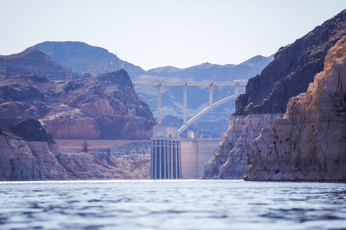 Hoover Dam intake towers and arched bridge framed by rugged desert canyon cliffs above calm Lake Mead water