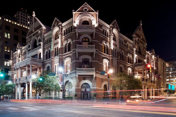 Historic ornate brick theater on a downtown corner at night, warm architectural lighting and balconies with colorful car light trails streaking across a busy intersection