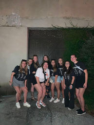 Smiling group of friends in casual summer outfits posing at night in front of a rustic wooden doorway and ivy-covered wall