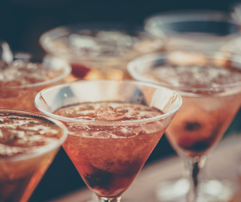 Close-up of chilled orange cocktails in martini glasses with crushed ice and berries on a bar, summer happy hour vibe