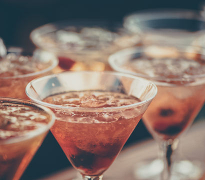 Close-up of chilled orange cocktails in martini glasses with crushed ice and berries on a bar, summer happy hour vibe