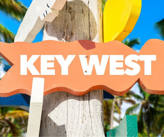 Bright colorful wooden sign reading KEY WEST mounted on a weathered post with palm trees and blue sky in Key West, Florida.