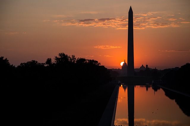 Sunset silhouette of the Washington Monument and Reflecting Pool on the National Mall in Washington, D.C., glowing orange sky with the sun setting behind the Capitol dome.