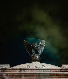 Bronze eagle statue with wings spread perched on a globe crowning a stone pediment carved with the letters D A R, set against a dramatic green-tinted night sky with swirling clouds.