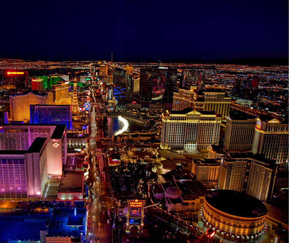 Aerial night view of the glittering Las Vegas Strip in Nevada, with brightly lit hotels and casinos, neon signs, a glowing fountain and a busy illuminated boulevard.