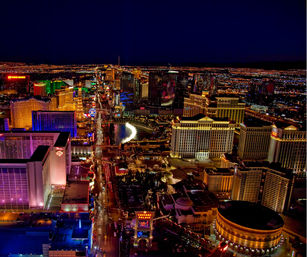 Aerial night view of the glittering Las Vegas Strip in Nevada, with brightly lit hotels and casinos, neon signs, a glowing fountain and a busy illuminated boulevard.