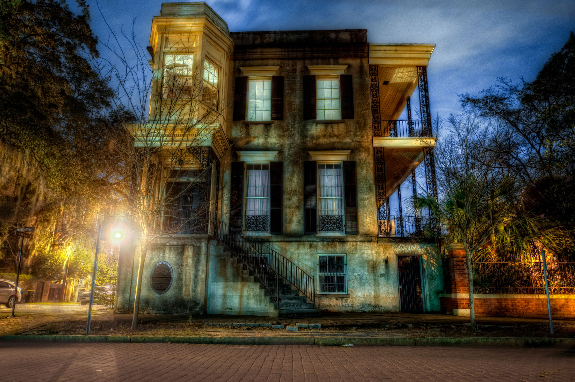 Warmly lit historic Southern townhouse with wrought-iron balconies, exterior staircase and Spanish moss at dusk