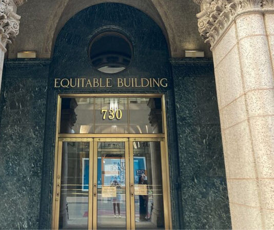 Historic downtown office entrance with arched dark green marble surround, carved stone columns, brass-framed glass double doors, and gold address number 730 above the doorway.