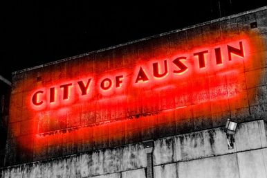 Glowing red "City of Austin" neon sign on a weathered concrete municipal building at night, gritty urban downtown vibe