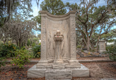Serene marble angel statue cradling a single red rose at a carved cemetery memorial beneath Spanish-moss draped live oaks