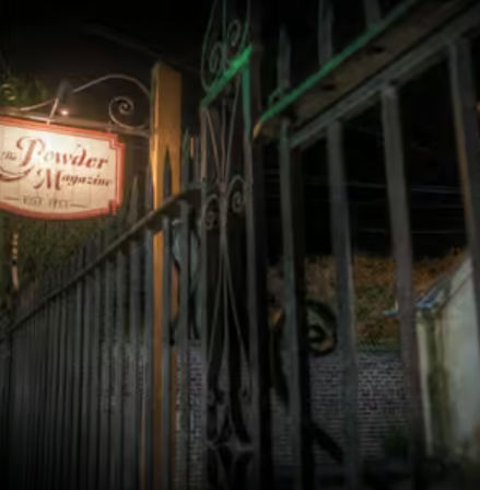 Night shot of ornate wrought-iron gate and vintage hanging sign at a historic district entrance