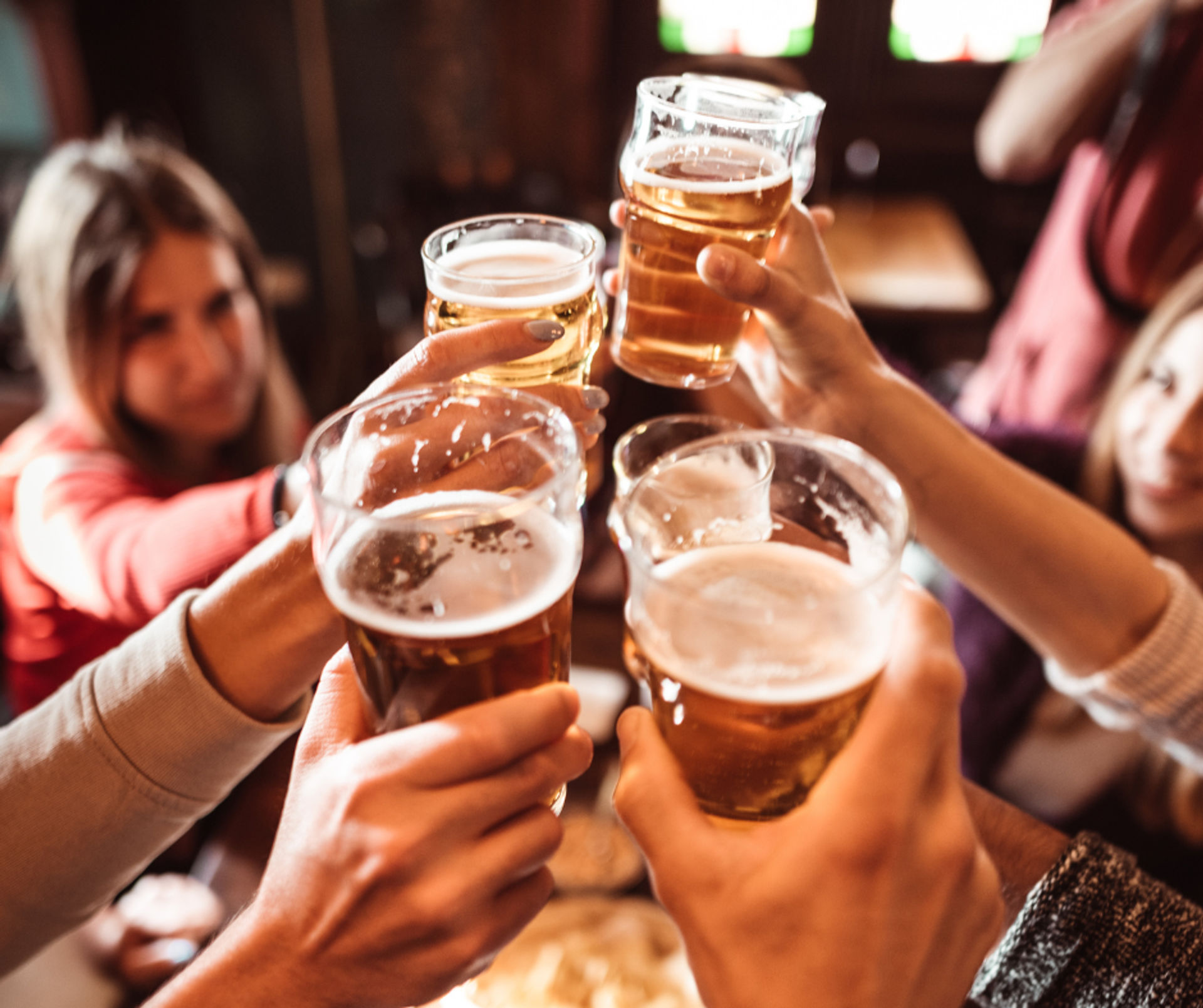 Cheers! Group of friends clinking pint glasses of amber beer at a cozy neighborhood pub