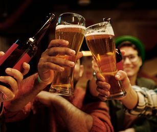 Group of friends toasting with tall amber beer glasses and bottles in a warm, dimly lit pub — cheers to a night out.