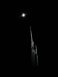 Dramatic moonlit church steeple silhouette with a glowing moon in a pitch-black night sky, Gothic spire and cross faintly illuminated.
