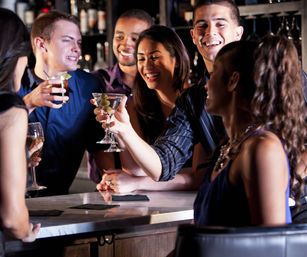 Young friends laughing and clinking martini glasses at a lively urban cocktail bar on a night out