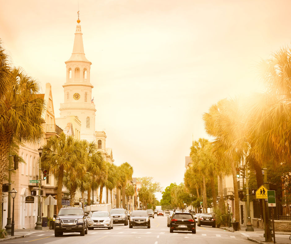 Golden-hour southern coastal downtown street lined with palm trees, historic white church steeple and cars driving along a busy avenue.