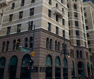 Historic multi-story stone corner building with arched ground-floor windows, green awnings, traffic lights and a Stout St street sign at the intersection