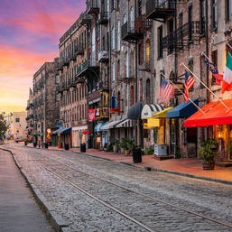 Sunset over a historic cobblestone street with tram rails, brick buildings, colorful awnings and waving flags.