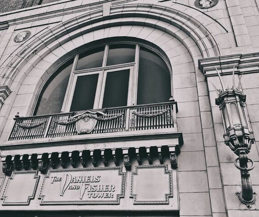 Historic downtown building façade with a large arched window, ornate iron balcony, carved stone cornice and vintage wall lantern — classic urban architectural detail.