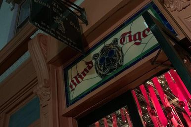 Whimsical stained-glass tiger wearing blue sunglasses mounted above a doorway, ornate architectural trim and red ribbon decorations visible at night.