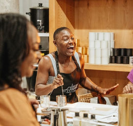 Cheerful instructor laughing and stirring a jar during a hands-on candle-making workshop in a cozy craft studio