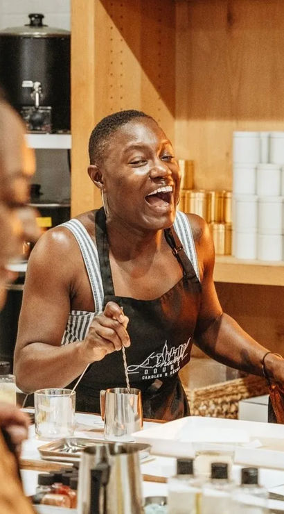 Cheerful instructor laughing and stirring a jar during a hands-on candle-making workshop in a cozy craft studio
