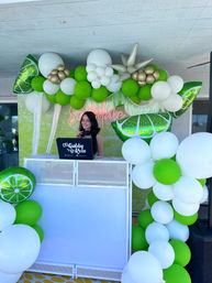 Smiling DJ at a white outdoor booth beneath a lime-green, white and gold balloon arch with lime-slice foil balloons and neon pink script backdrop