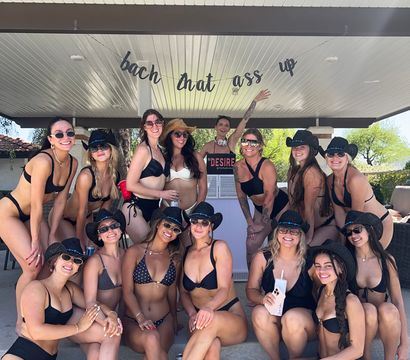 Sunlit poolside cabana bachelorette party: group of friends in black bikinis and cowboy hats posing together under a playful party banner
