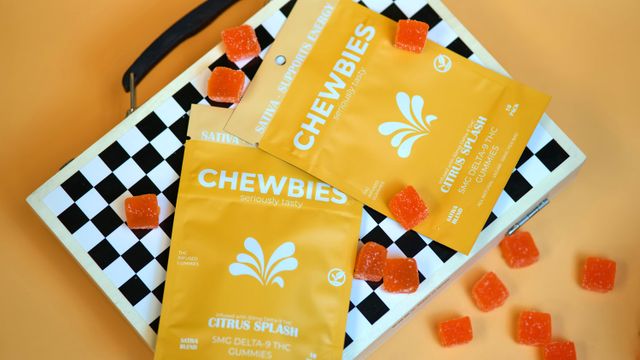 Flatlay of bright yellow packets of citrus THC gummies with scattered orange sugar-coated gummy squares on a black-and-white checkerboard case over an orange background