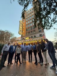 Smiling group posing at dusk under a glowing vintage theater marquee and tall brick building on a downtown Tampa sidewalk