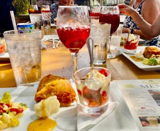 Vibrant outdoor patio table with ruby-red sangria in stemmed glasses, iced water, plated appetizers (fried bite and salad) and mini dessert cups