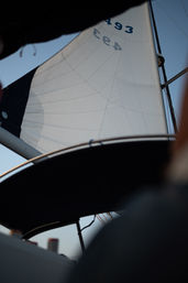 Sailboat cockpit view looking up at a billowing white mainsail and rigging against a clear blue sky.