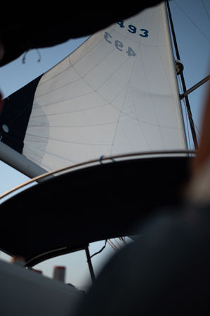 Sailboat cockpit view looking up at a billowing white mainsail and rigging against a clear blue sky.