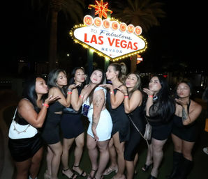 Group of women blowing kisses while posing in front of the glowing Welcome to Las Vegas, Nevada sign at night, lively nightlife photo.