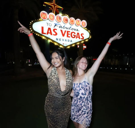 Two friends in patterned dresses smiling with arms raised at night in front of the iconic Welcome to Fabulous Las Vegas Nevada sign