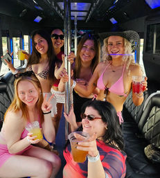 Six friends in swimsuits and summer outfits holding drinks and smiling around a pole inside a party bus, lively daytime bachelorette-style celebration.