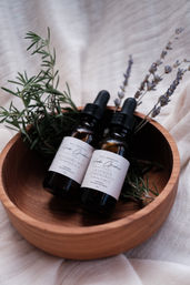 Two amber dropper bottles labeled rosemary mint and lavender lemongrass scalp oils nestled with fresh rosemary sprigs and dried lavender in a wooden bowl on soft linen — natural botanical skincare, herbal aromatherapy.