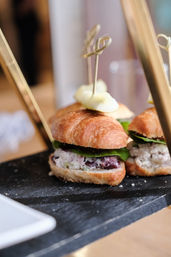 Mini croissant sandwich filled with creamy, grape-studded salad and baby greens, topped with decorative bamboo skewers and served on a black slate platter — brunch appetizer