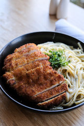 Crispy breaded chicken cutlet sliced over creamy garlic parmesan spaghetti with chopped parsley in a black bowl — Italian-style comfort pasta dish.