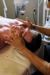 Man receiving a relaxing facial massage with cream as a therapist gently massages temples and cheeks on a towel-covered spa treatment table