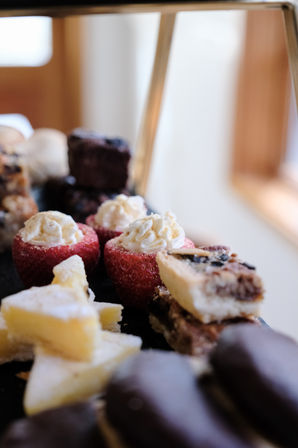 Close-up dessert platter with cream-filled strawberries, bite-sized pastry bars, lemon squares and chocolate-covered cookies on a black tray